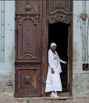 Foto de uma mulher praticante da Santería em frente a uma casa religiosa