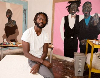 Foto do artista Amoako Boafo em frente algumas de suas pinturas