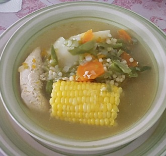 Foto de um prato com frango, legumes, milho cozido, num caldo. 