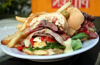 Foto de um sanduiche com carne, ovo, batata frita, tomate e outros ingredientes