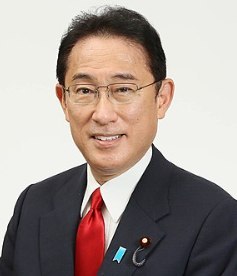 Foto de um homem japonês de cabelo curto preto, sorrindo, usando óculos.