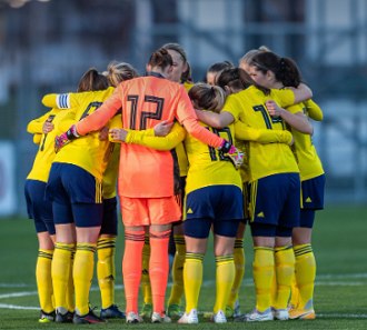 Foto de jogadoras de futebol em circulo, abra&ccedil;adas.