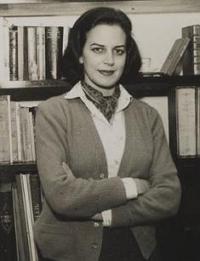 Lygia Fagundes Telles, escritora brasileira, em pé de braços cruzados em frente uma estante de livros