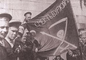 Foto antiga mostrando marinheiros segurando uma bandeira com uma foice, um crânio e uma lança desenhados.