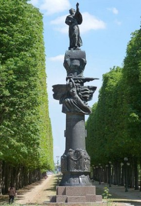 Monumento cercado de árvores composto de uma coluna cinza com uma figura de uma pessoa na parte superior