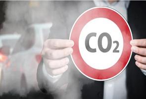 Homem segurando uma placa indicando CO2 no trânsito com fumaça.